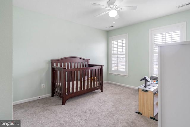 carpeted bedroom featuring visible vents, ceiling fan, a crib, and baseboards