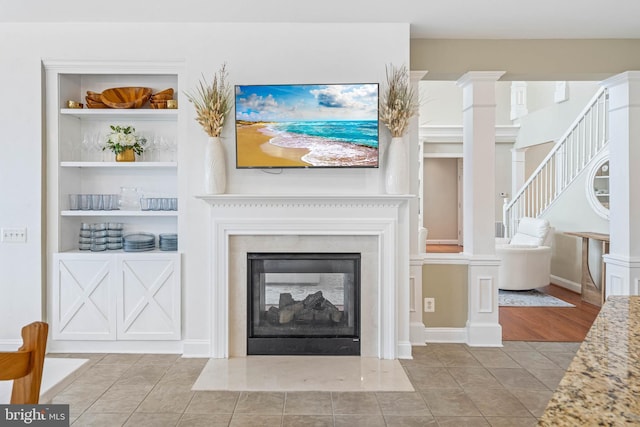 unfurnished living room featuring built in shelves, baseboards, a multi sided fireplace, tile patterned flooring, and ornate columns