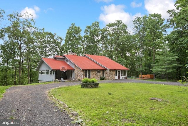 view of front of home featuring driveway, stone siding, a chimney, and a front lawn