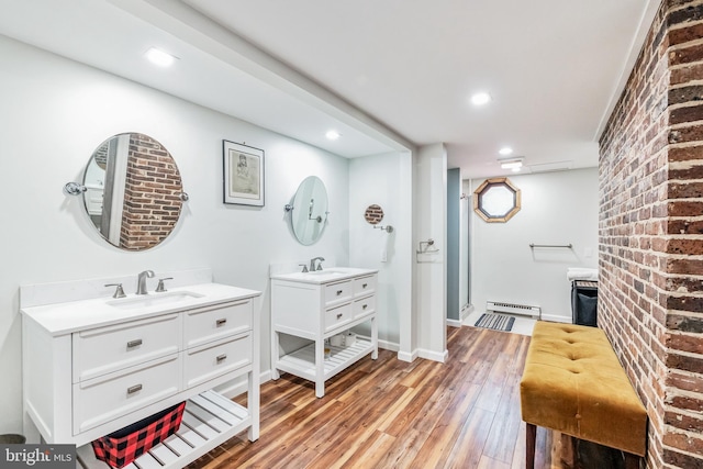 bathroom with wood finished floors, baseboard heating, two vanities, and a sink