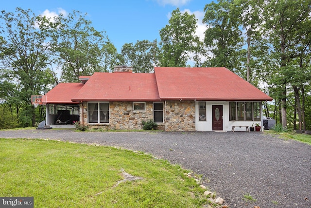 view of front facade with gravel driveway, a chimney, a front yard, a sunroom, and an attached carport