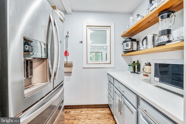 kitchen with open shelves, light countertops, light wood-type flooring, stainless steel fridge, and baseboards