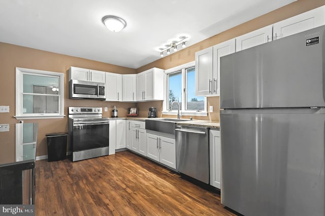 kitchen featuring dark wood finished floors, stainless steel appliances, light countertops, white cabinetry, and a sink