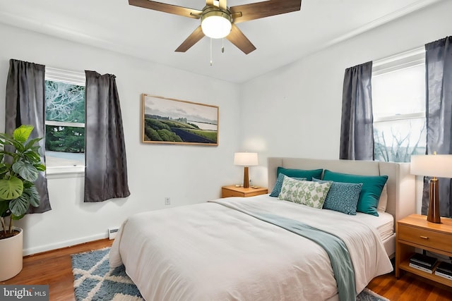 bedroom with ceiling fan, a baseboard heating unit, wood finished floors, and baseboards