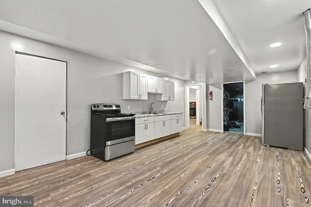 kitchen with light wood finished floors, stainless steel appliances, white cabinets, a sink, and baseboards