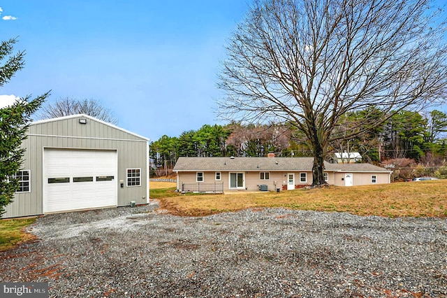 view of front of home with a front yard, an outdoor structure, a detached garage, and gravel driveway