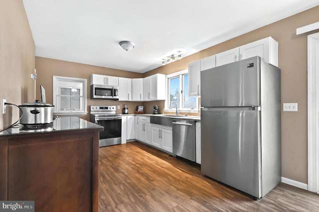 kitchen with dark wood-style flooring, stainless steel appliances, white cabinetry, a sink, and baseboards