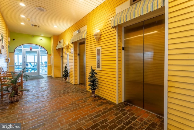 hall with wooden ceiling, brick floor, recessed lighting, visible vents, and elevator