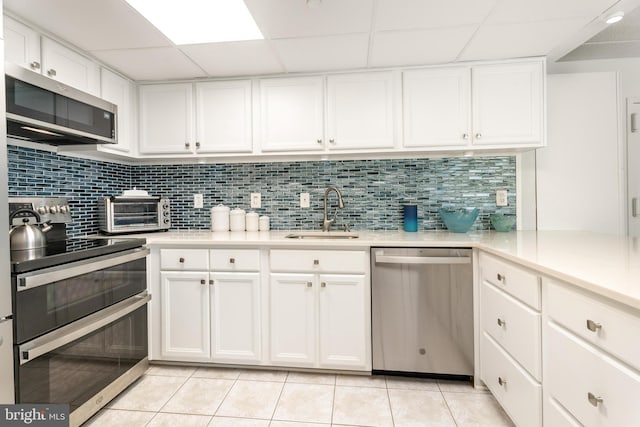 kitchen with light tile patterned floors, decorative backsplash, appliances with stainless steel finishes, white cabinets, and a sink