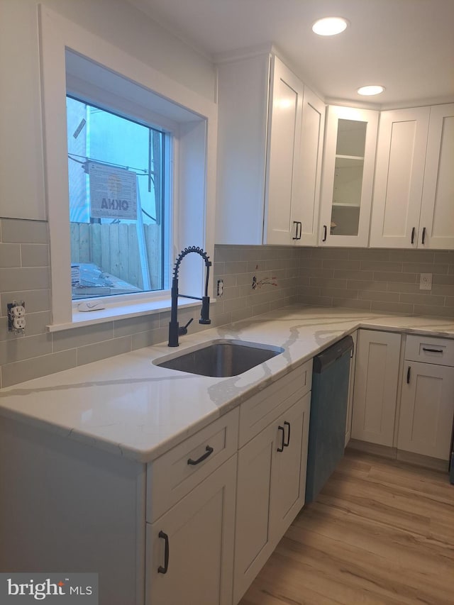 kitchen with white cabinets, a sink, light stone countertops, light wood-type flooring, and dishwashing machine