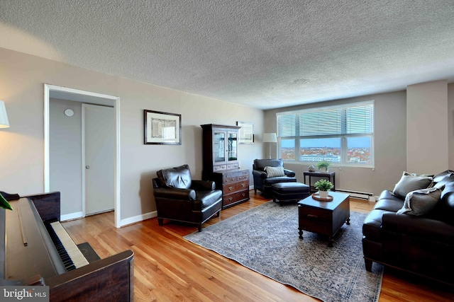 living area featuring a baseboard heating unit, a textured ceiling, light wood-style flooring, and baseboards