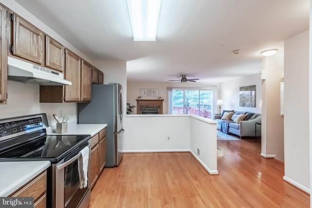 kitchen featuring under cabinet range hood, a fireplace, open floor plan, appliances with stainless steel finishes, and light wood finished floors