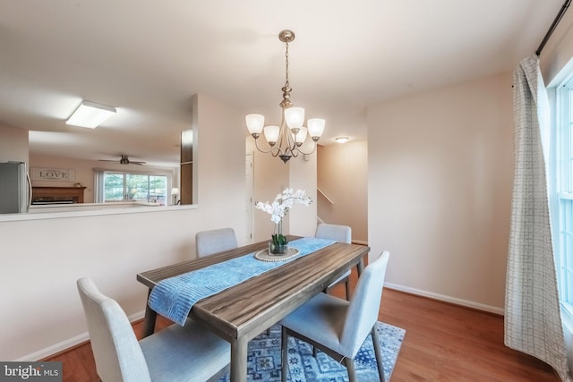 dining room featuring ceiling fan with notable chandelier, wood finished floors, and baseboards