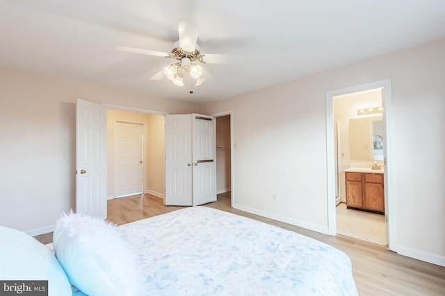 bedroom with light wood finished floors, a closet, ensuite bathroom, a sink, and baseboards