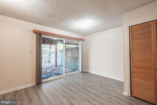 unfurnished room with a textured ceiling, wood finished floors, and baseboards