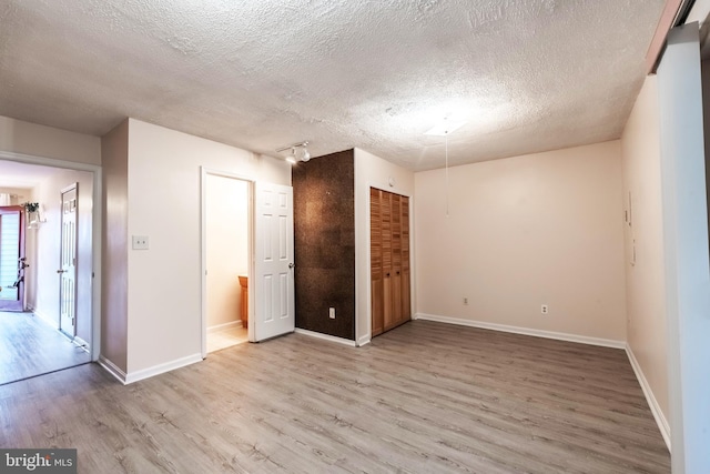 unfurnished room with a textured ceiling, light wood finished floors, and baseboards