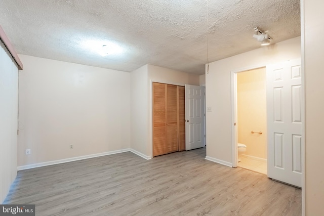 unfurnished bedroom featuring a textured ceiling, ensuite bathroom, baseboards, a closet, and light wood finished floors