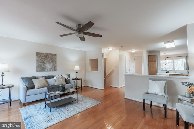 living room featuring ceiling fan with notable chandelier, light wood-style flooring, and baseboards