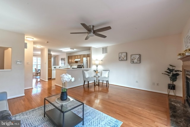 living area with visible vents, baseboards, a fireplace with flush hearth, ceiling fan, and light wood-type flooring