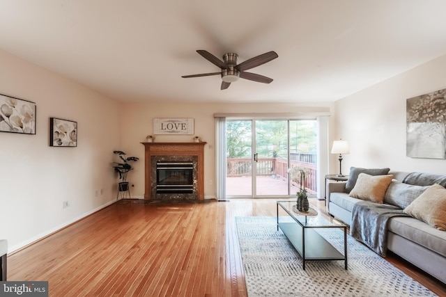 living area with ceiling fan, a premium fireplace, wood finished floors, and baseboards