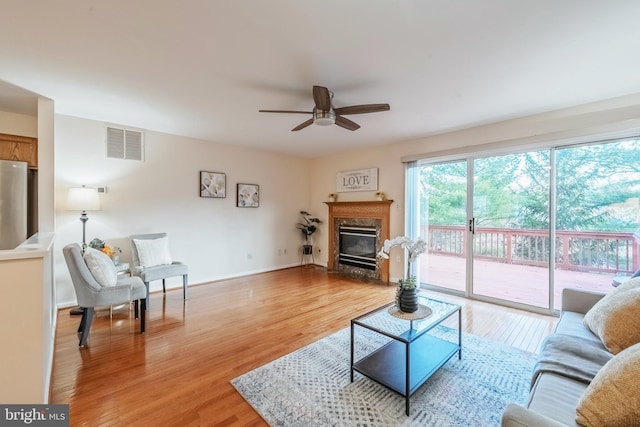 living room featuring visible vents, light wood-style flooring, a premium fireplace, ceiling fan, and baseboards