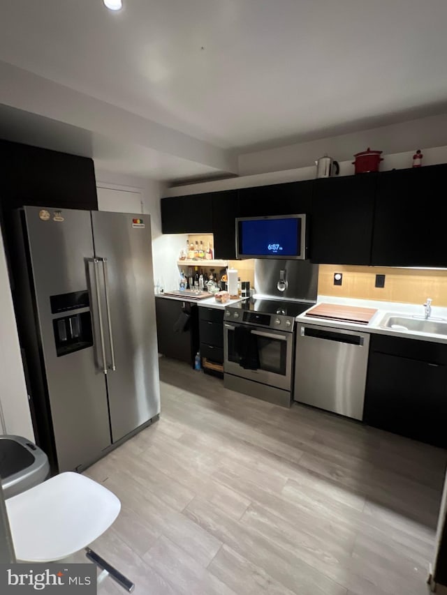 kitchen with dark cabinetry, appliances with stainless steel finishes, light countertops, and a sink