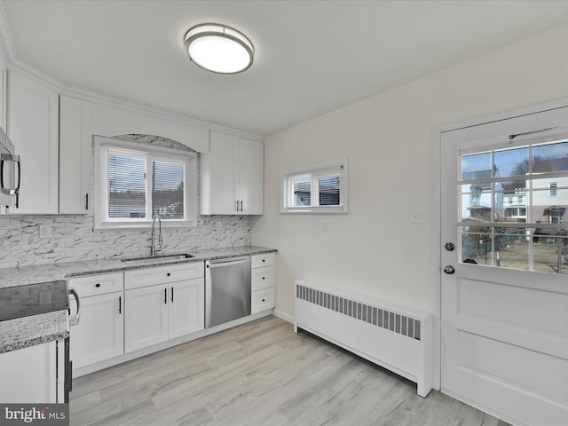 kitchen with radiator heating unit, white cabinetry, a sink, and stainless steel dishwasher