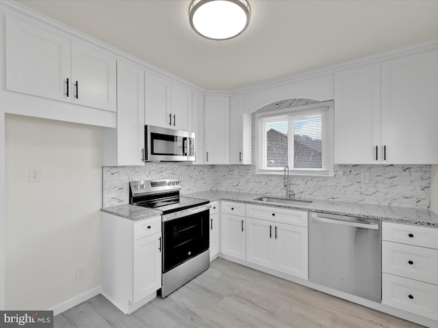 kitchen featuring decorative backsplash, appliances with stainless steel finishes, light stone counters, white cabinetry, and a sink