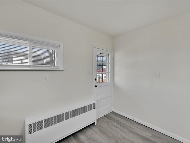 spare room featuring baseboards, light wood-type flooring, and radiator