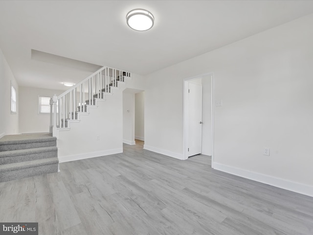 unfurnished living room with stairs, baseboards, and wood finished floors