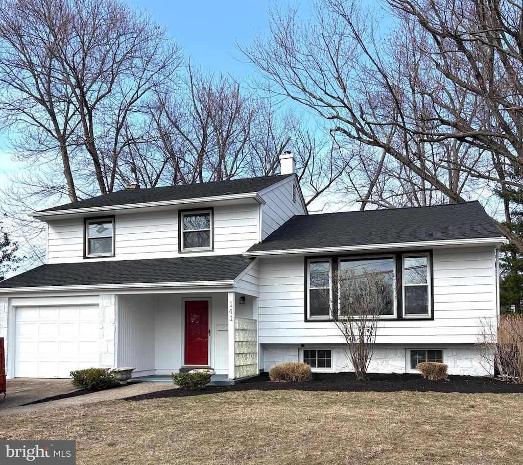 split level home featuring roof with shingles, a chimney, and a front yard