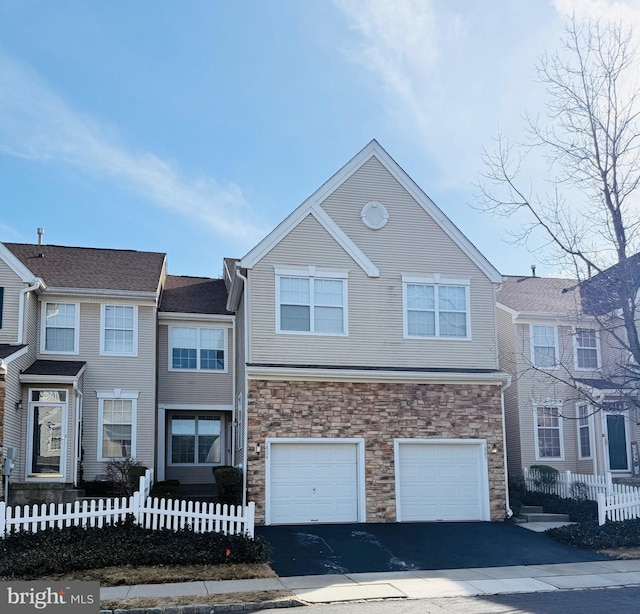 townhome / multi-family property with driveway, stone siding, and a fenced front yard