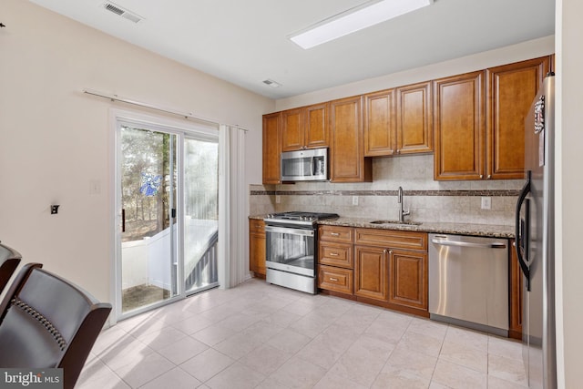 kitchen featuring tasteful backsplash, appliances with stainless steel finishes, brown cabinetry, a sink, and light stone countertops