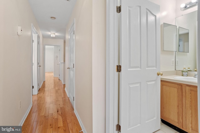 corridor with light wood-style flooring, baseboards, and a sink