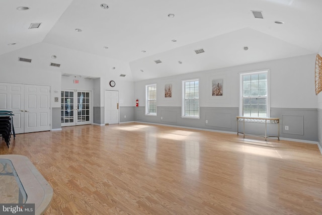 unfurnished living room featuring lofted ceiling, a wainscoted wall, visible vents, and light wood finished floors