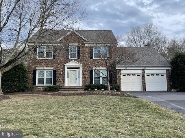 colonial-style house with brick siding, aphalt driveway, a front lawn, and an attached garage