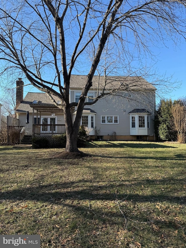 rear view of house with a deck, a chimney, and a yard