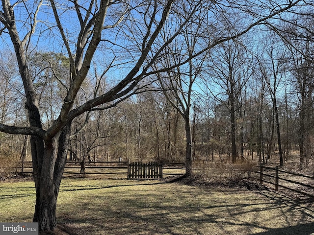 view of property's community featuring a view of trees, a lawn, and fence