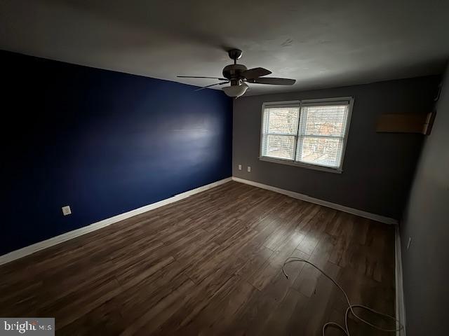 unfurnished room featuring a ceiling fan, dark wood finished floors, and baseboards