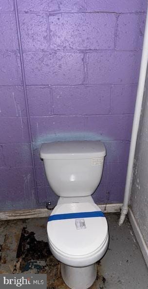 bathroom with unfinished concrete flooring, toilet, and concrete block wall