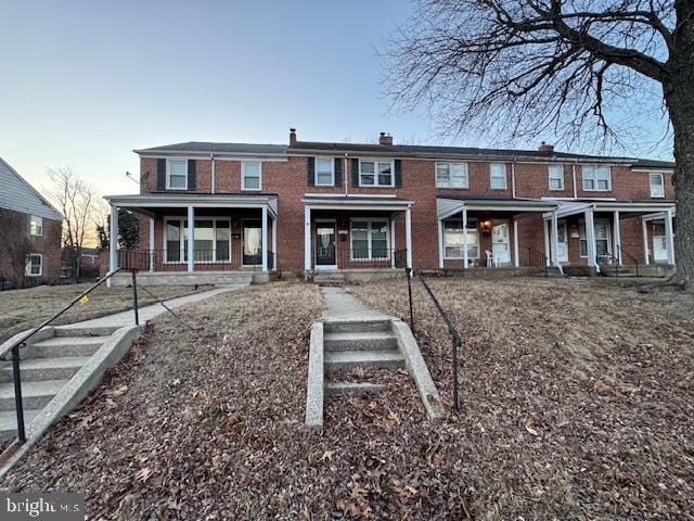 townhome / multi-family property featuring covered porch and brick siding