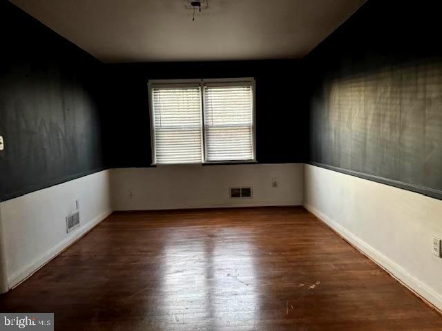 spare room featuring baseboards, visible vents, and wood finished floors