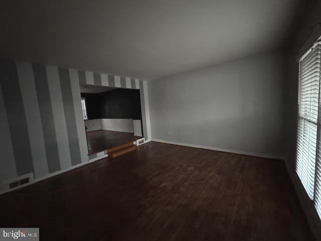 unfurnished room with dark wood-style flooring, visible vents, and baseboards