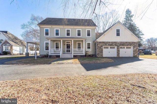 colonial house with a porch, stone siding, a garage, and driveway