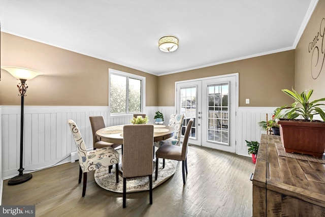 dining area with french doors, a wainscoted wall, crown molding, and wood finished floors