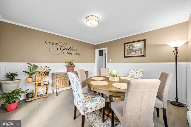 dining space with a wainscoted wall, wood finished floors, and crown molding