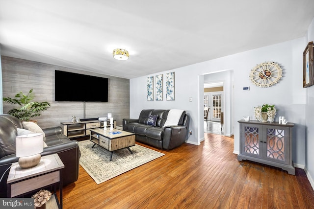 living room featuring an accent wall, wood-type flooring, and baseboards