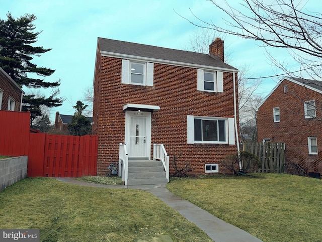 view of front of home with brick siding, a chimney, a front lawn, and fence