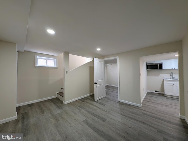 basement featuring a sink, stairway, baseboards, and wood finished floors