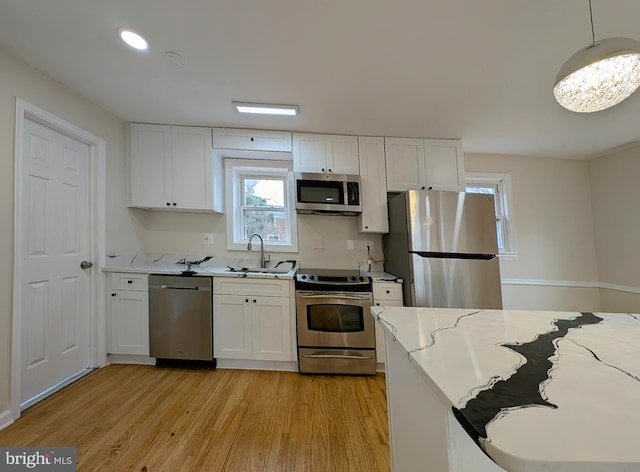 kitchen with stainless steel appliances, light wood-style floors, a sink, and white cabinets